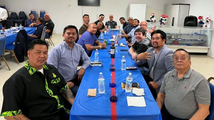 Members share a meal at a long table with a blue tablecloth in a lodge dining room, smiling for the camera.